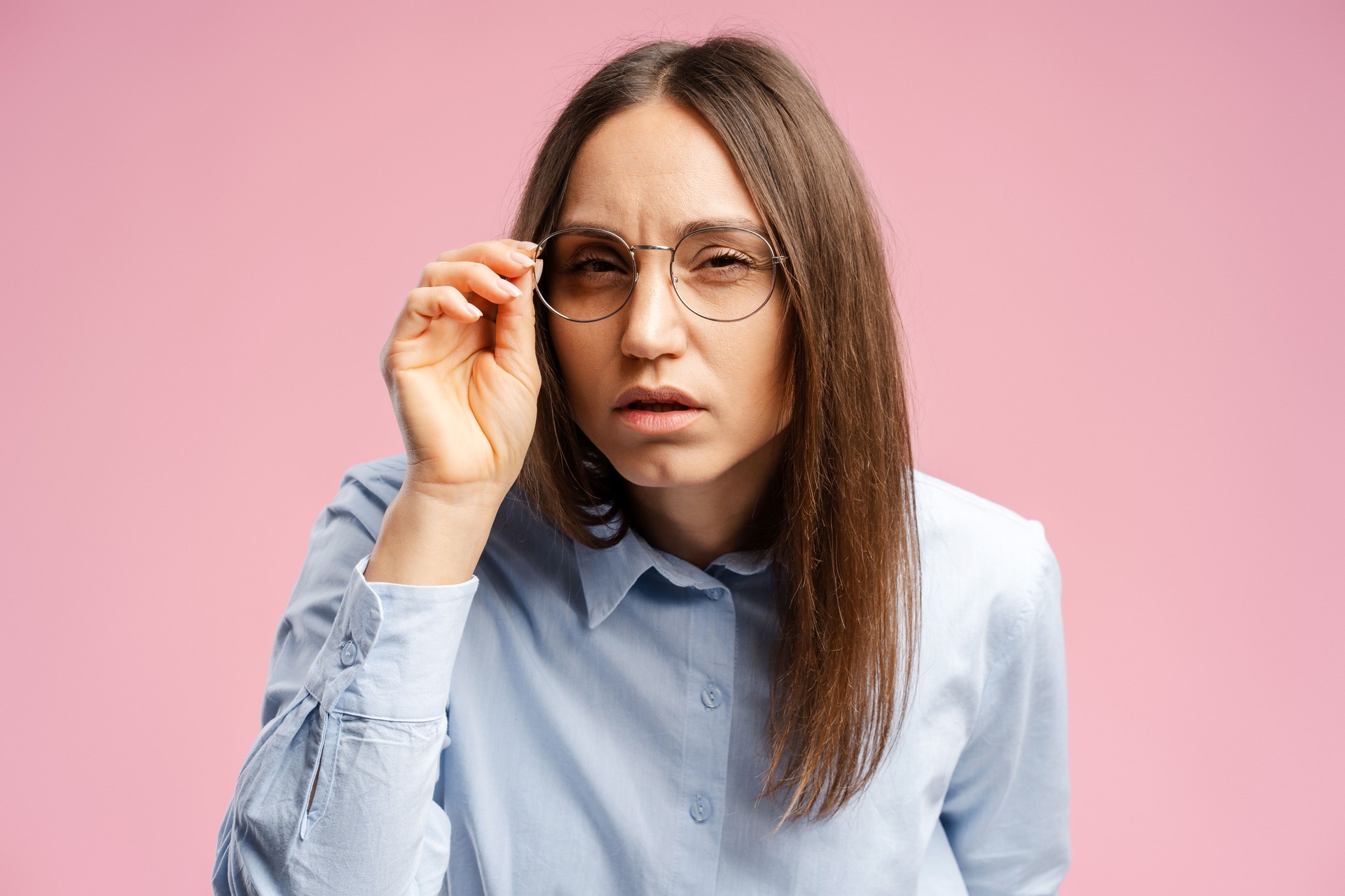 Serious-looking focused woman frowning and squinting as looking at camera, touching glasses